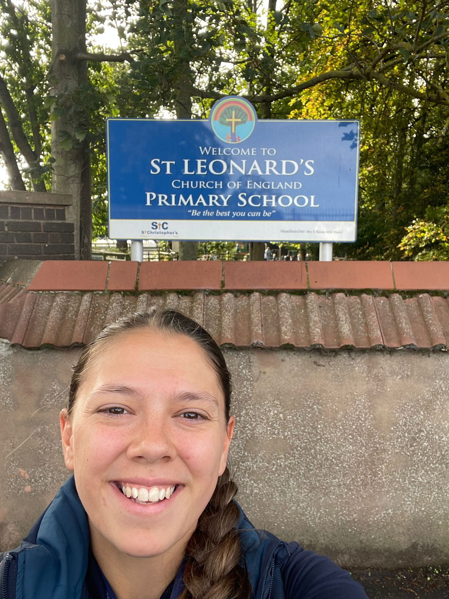 Bronwyn smiling in front of a sign for St Leonard's Primary School