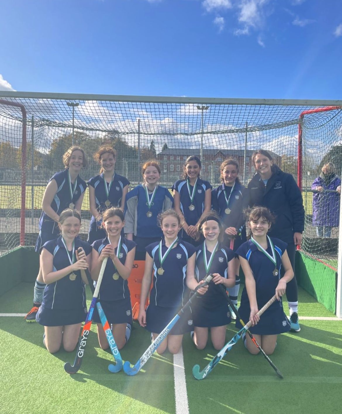 Girls holding hockey sticks in front of a net